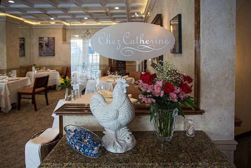 Chez Catherine dining room with view of plate glass with restaurants logo, chicken and flowers decoration