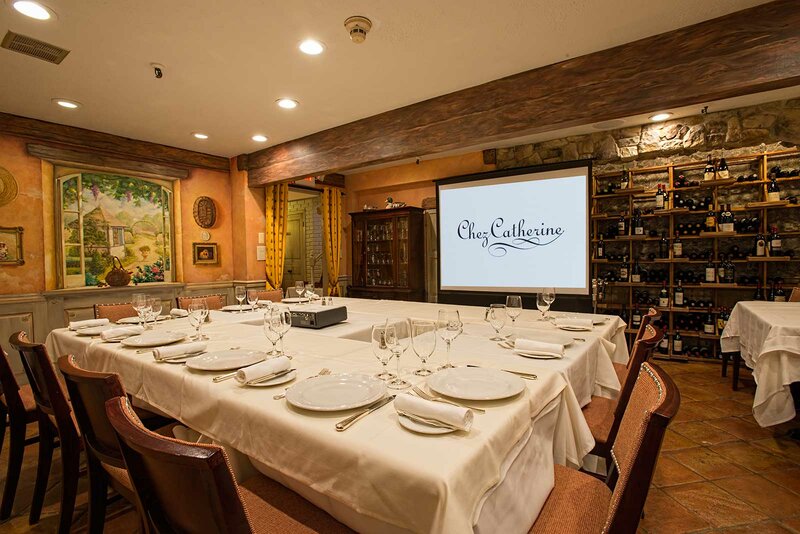 Private dining room with set tables and projection of Chez Catherine logo on projector screen